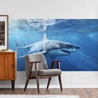 A wall decal of a great white shark swimming in the ocean applied to a wall with a chair and side table in the foreground. 