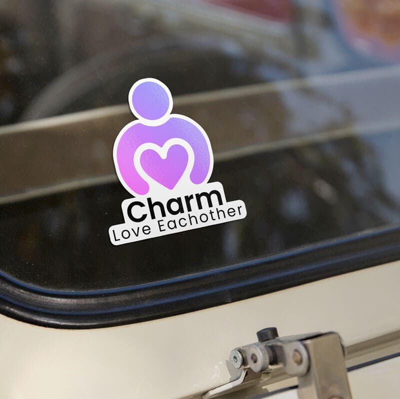 Car window with a 'Charm Love Each Other' sticker featuring a purple heart icon, placed on a cream-colored vehicle.