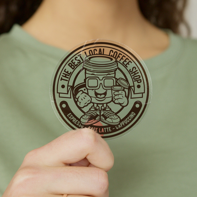 Person holding a round clear sticker with a coffee shop logo, showing its transparent design.